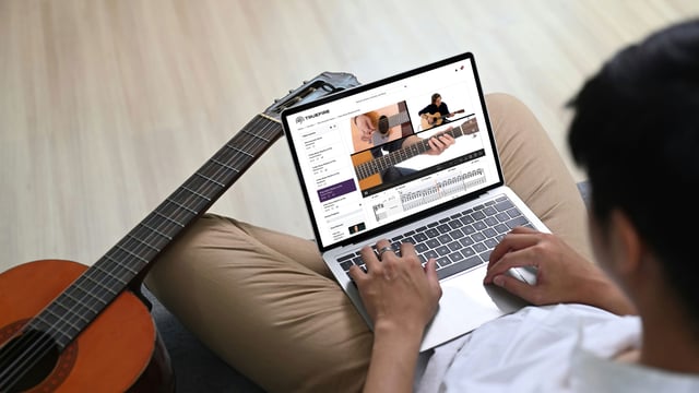 Guitarist playing lead on an electric guitar through an amp during a TrueFire online lesson with interactive tab on screen